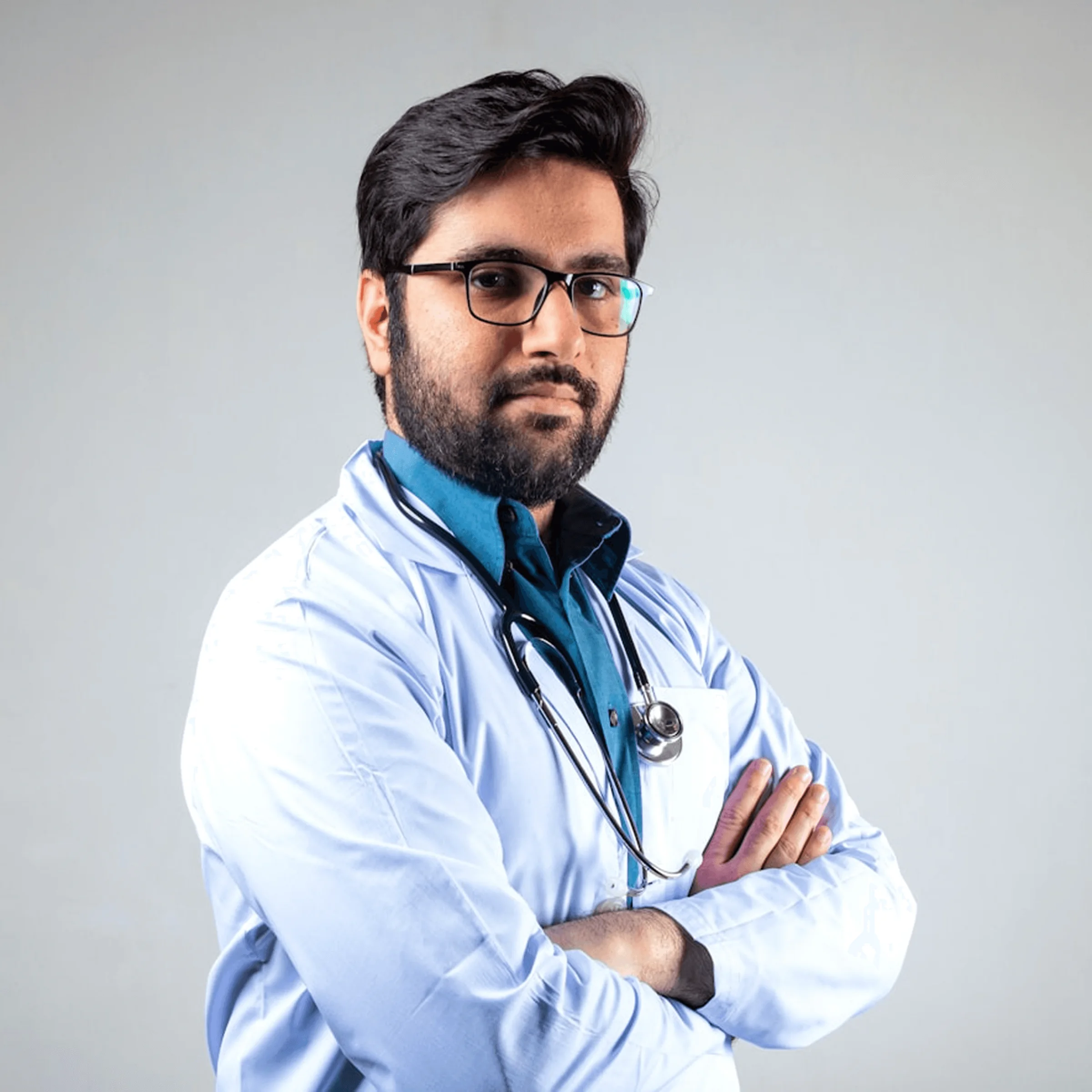 Doctor with glasses and beard in white coat, arms crossed against light gray background