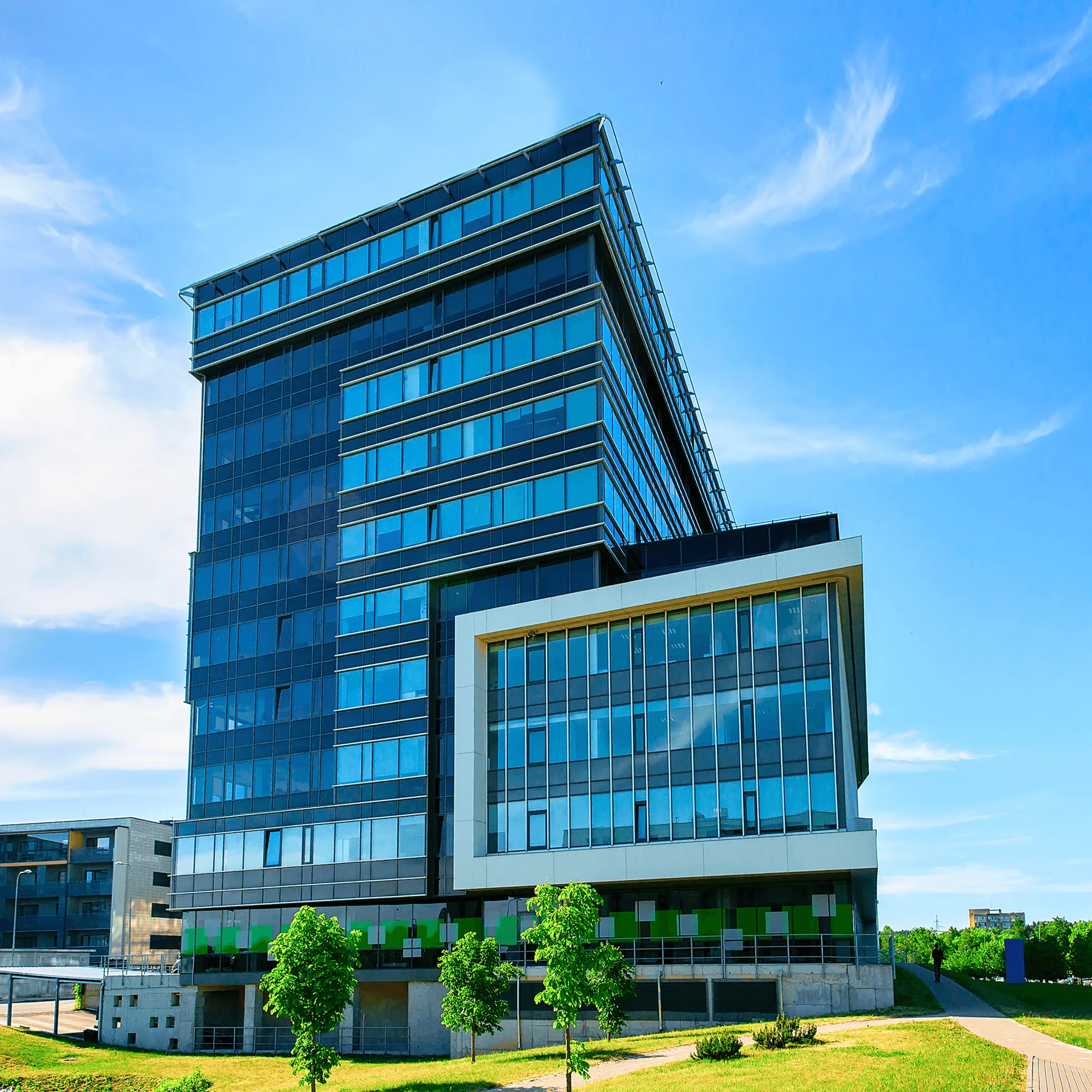 Modern glass office building with white framing, lawn, trees, and clear sky