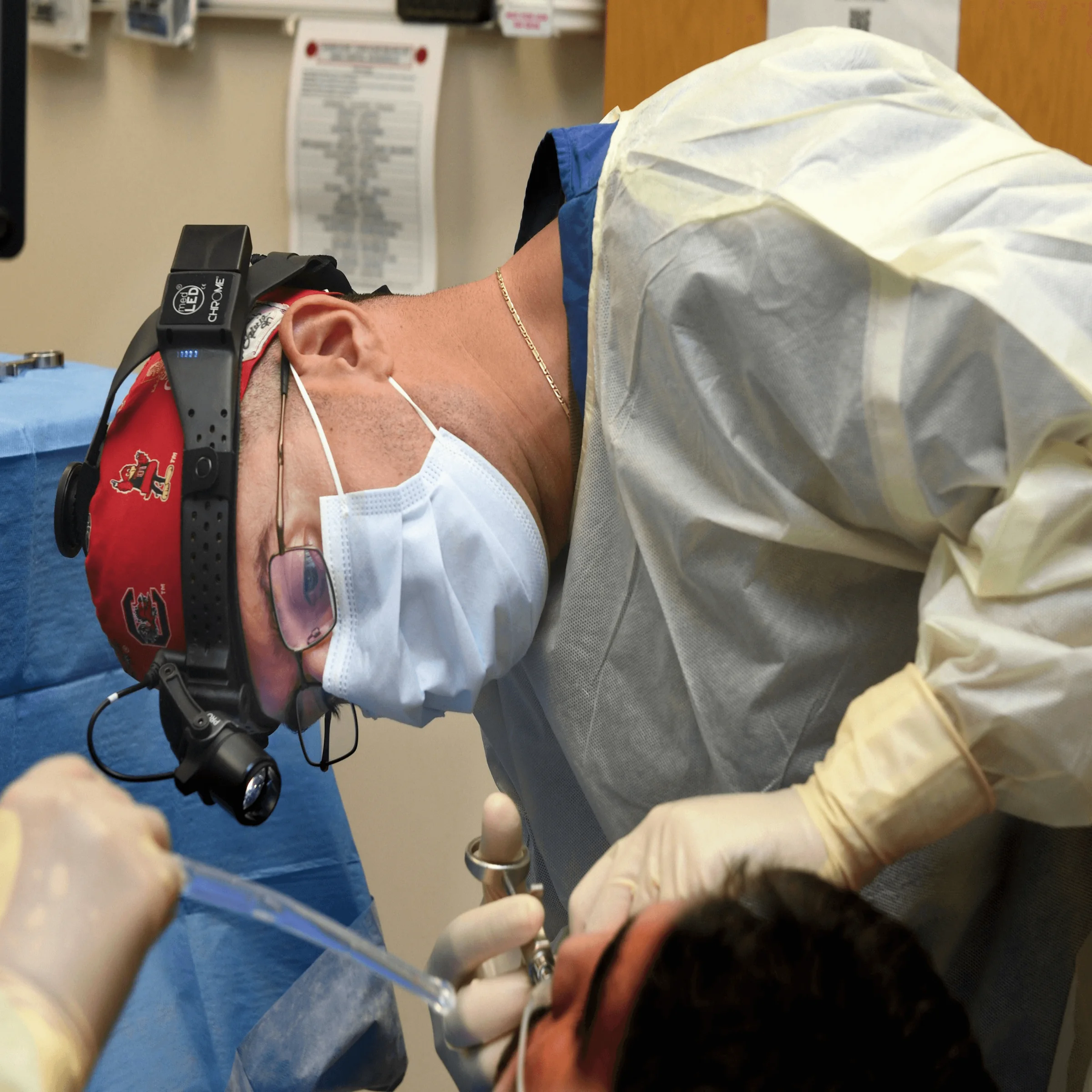 Dental professional in mask and headlamp performing oral procedure on patient in clinical setting
