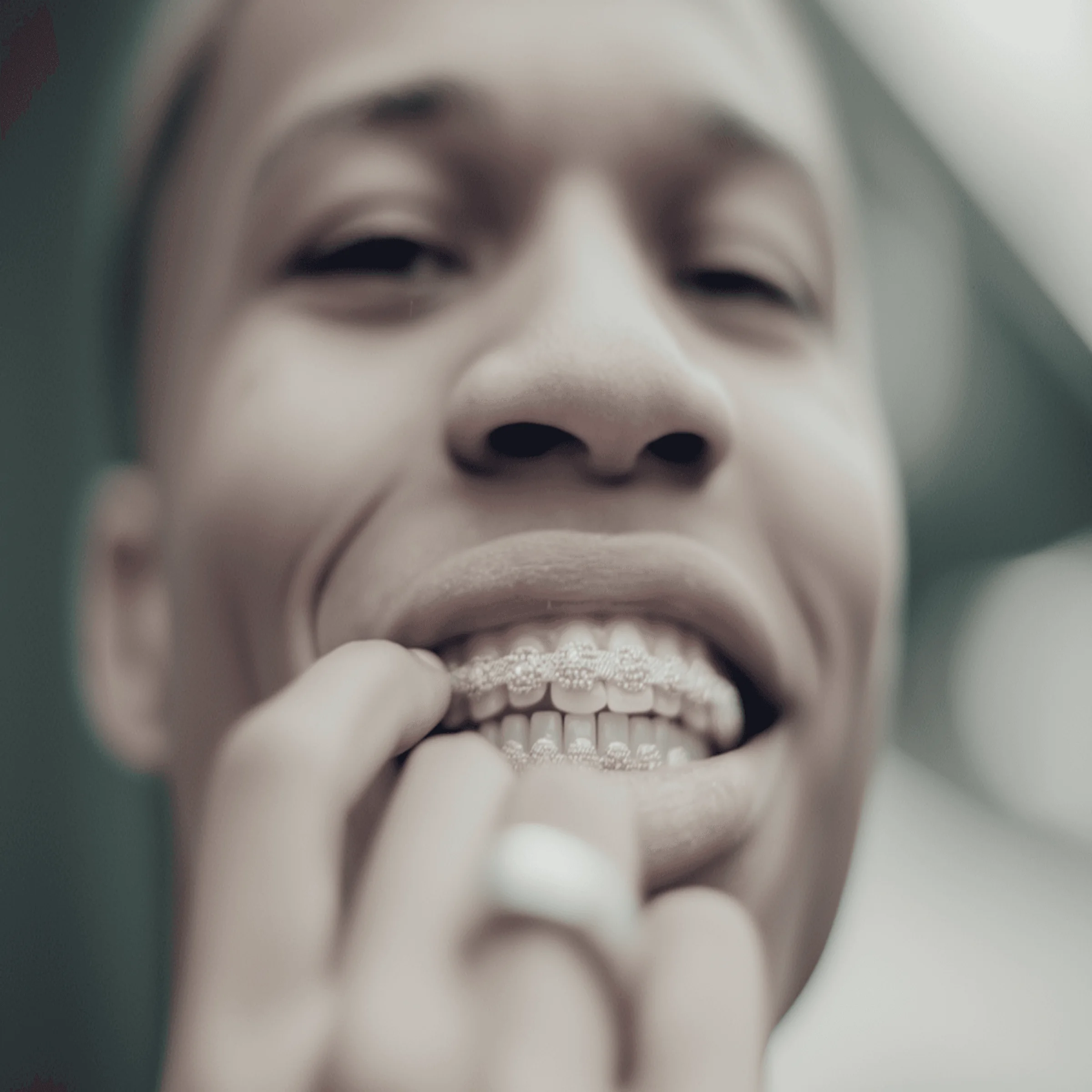 Close-up of smiling person wearing decorative dental grills and ring, with blurred background.